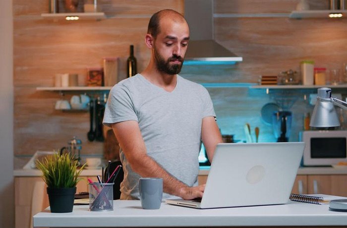 Mutfak masasında bilgisayar ile çalışan bir adam