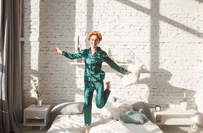 Yatağın üzerinde zıplayan yeşil pijamalı kadın