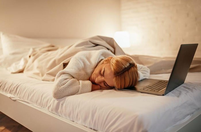 Bilgisayar başındayken yatağında uyuyan bir kadın