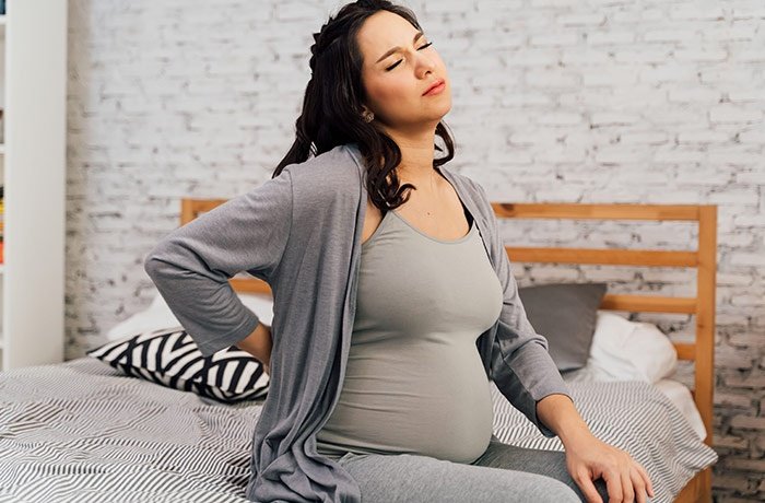 Yatakta otururken belini tutan hamile bir kadın