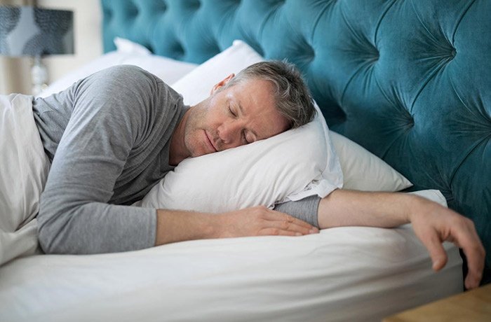 Bir elini yastığın altına koyan uykuda bir adam